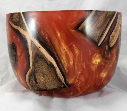 Red and orange epoxy bowl with suspended wood inclusions.
